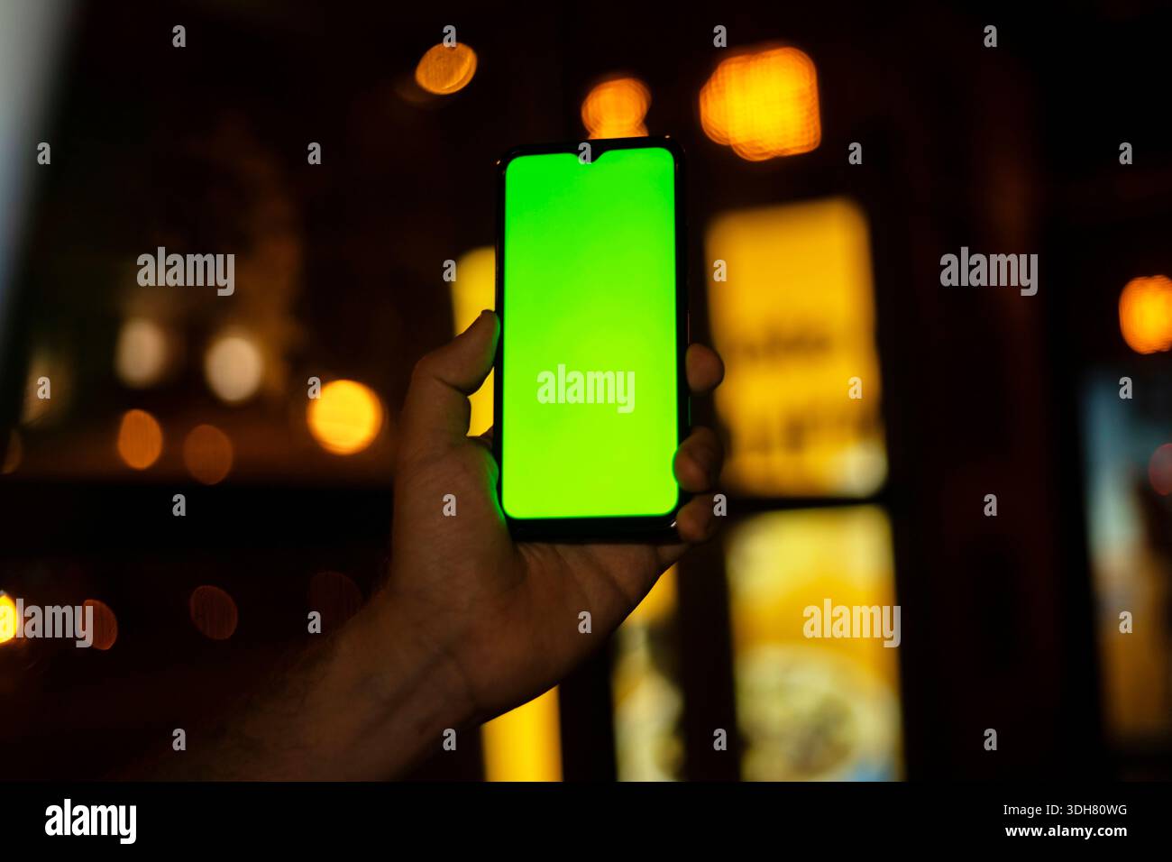main tenant le téléphone cellulaire avec écran sur l'appareil photo dans la ville la nuit avec les feux de voiture en arrière-plan Banque D'Images