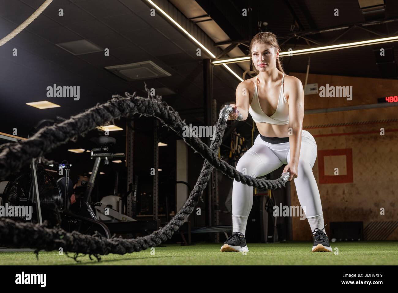 Athlète féminine utilisant des cordes de combat sur le gazon de gymnastique pour le conditionnement de force, pour les bannières de site Web ou les annonces sociales. Banque D'Images