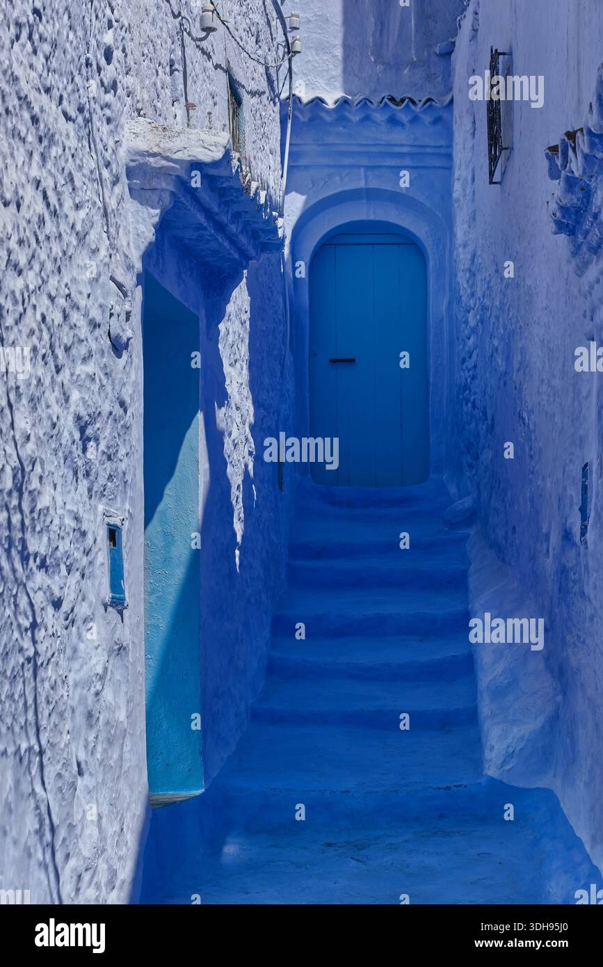 064 ruelle piétonne étroite, étagée, inclinée peinte dans des tons de bleu - peut-être le plus bleu de la ville - menant à une porte en bois fermée. Chefchaouen-Maroc Banque D'Images