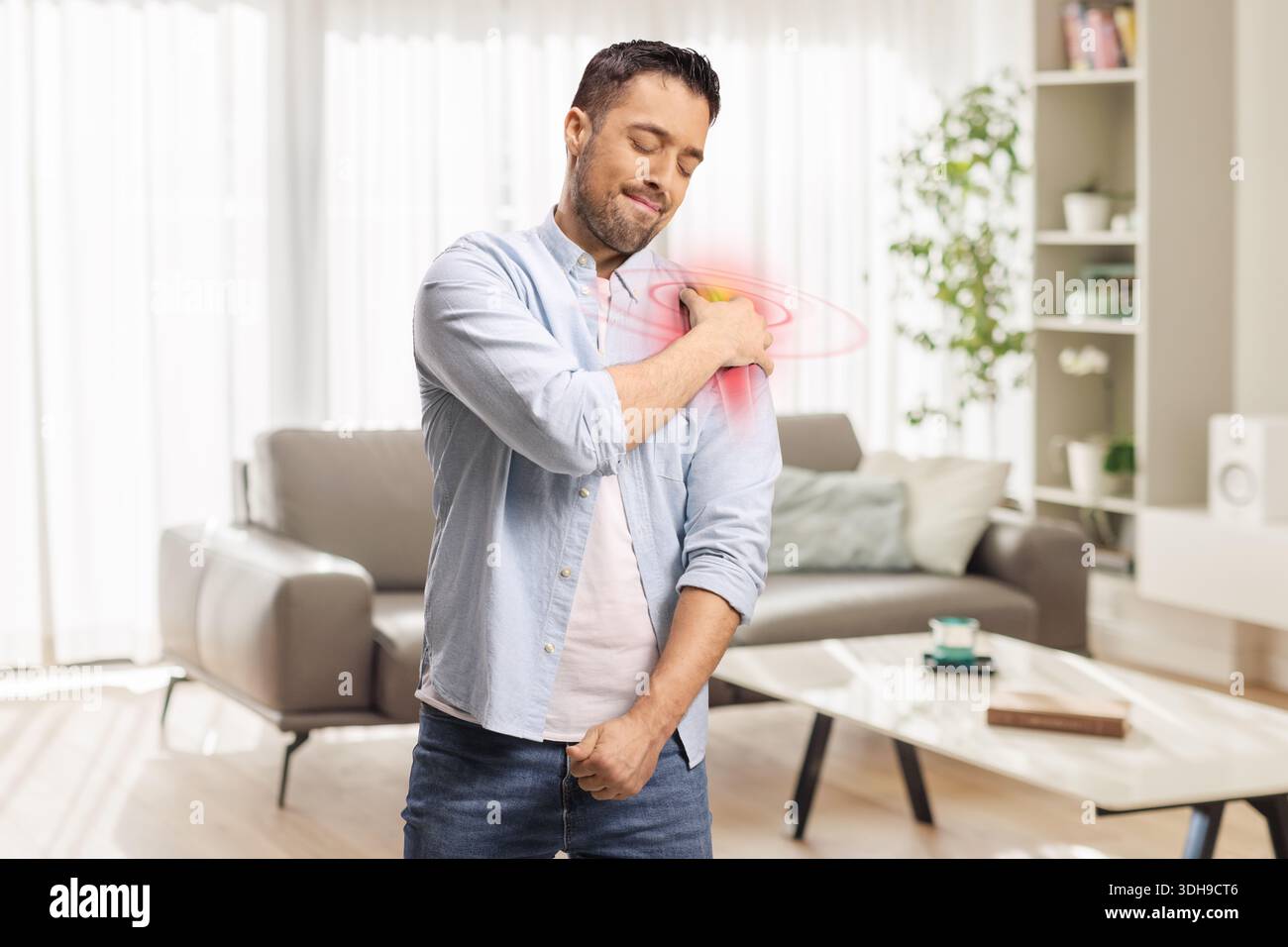 Jeune homme avec douleur à l'épaule tendue tenant son bras dans une pièce Banque D'Images