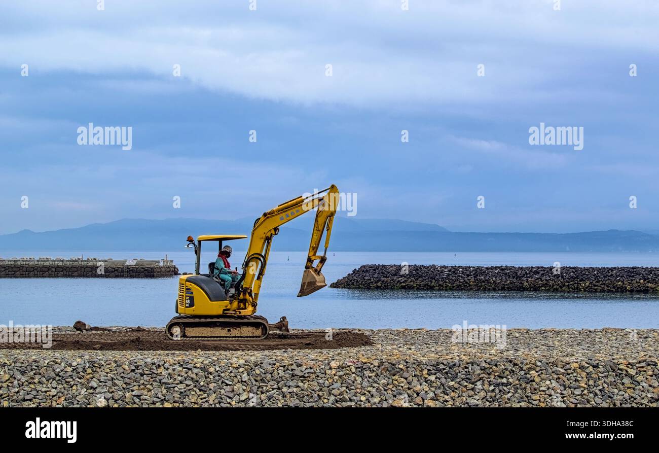 Ibusuki, Japon - mars 31 2022 : une excavatrice solitaire travaille sur un mur de soutènement près du rivage par un jour couvert à Ibusuki, Japon Banque D'Images