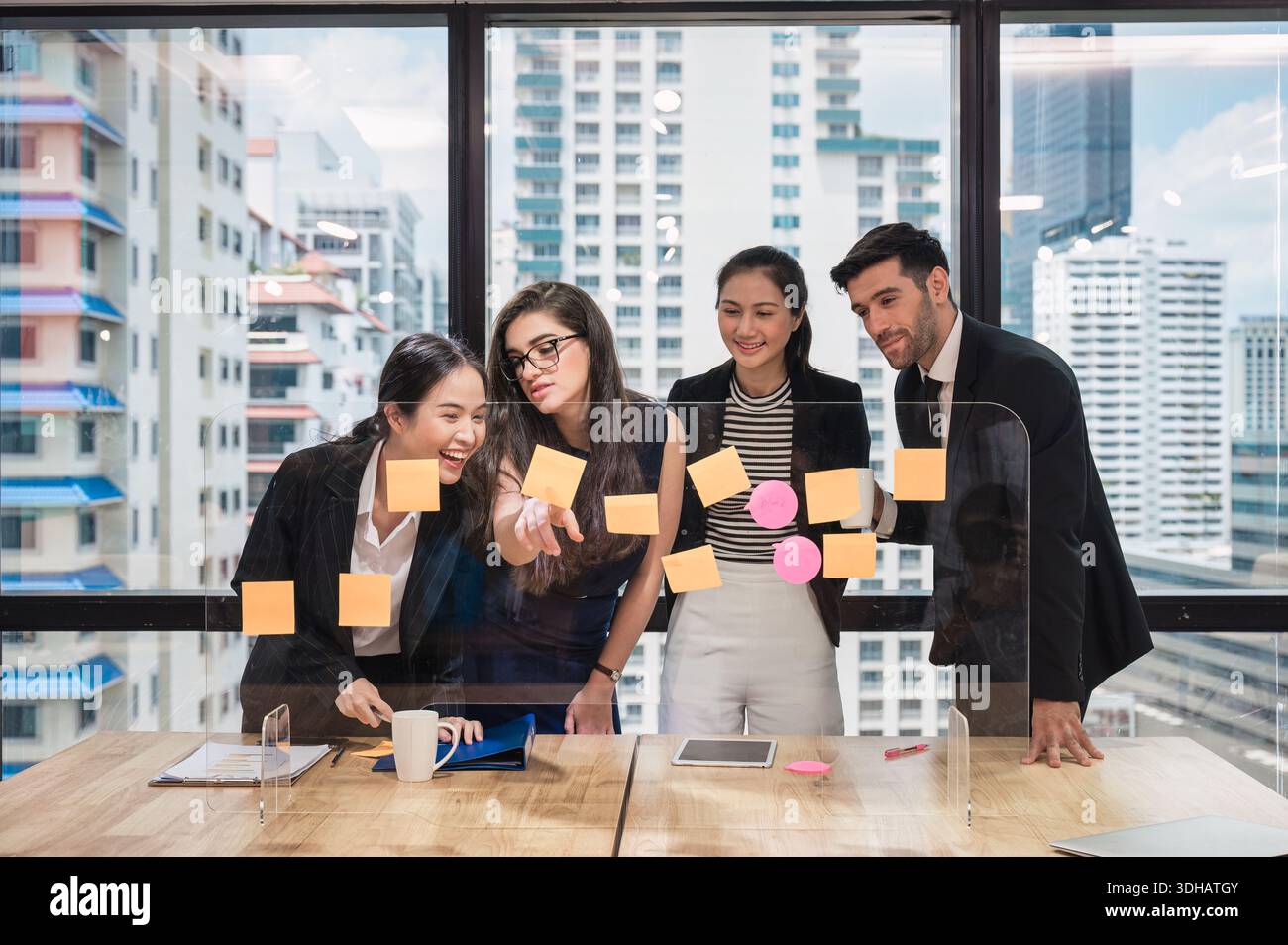 Groupe de collègues d'affaires multiethniques analysant et discutant de l'idée de projet d'entreprise avec la note collante collée à bord dans le bureau moderne Banque D'Images