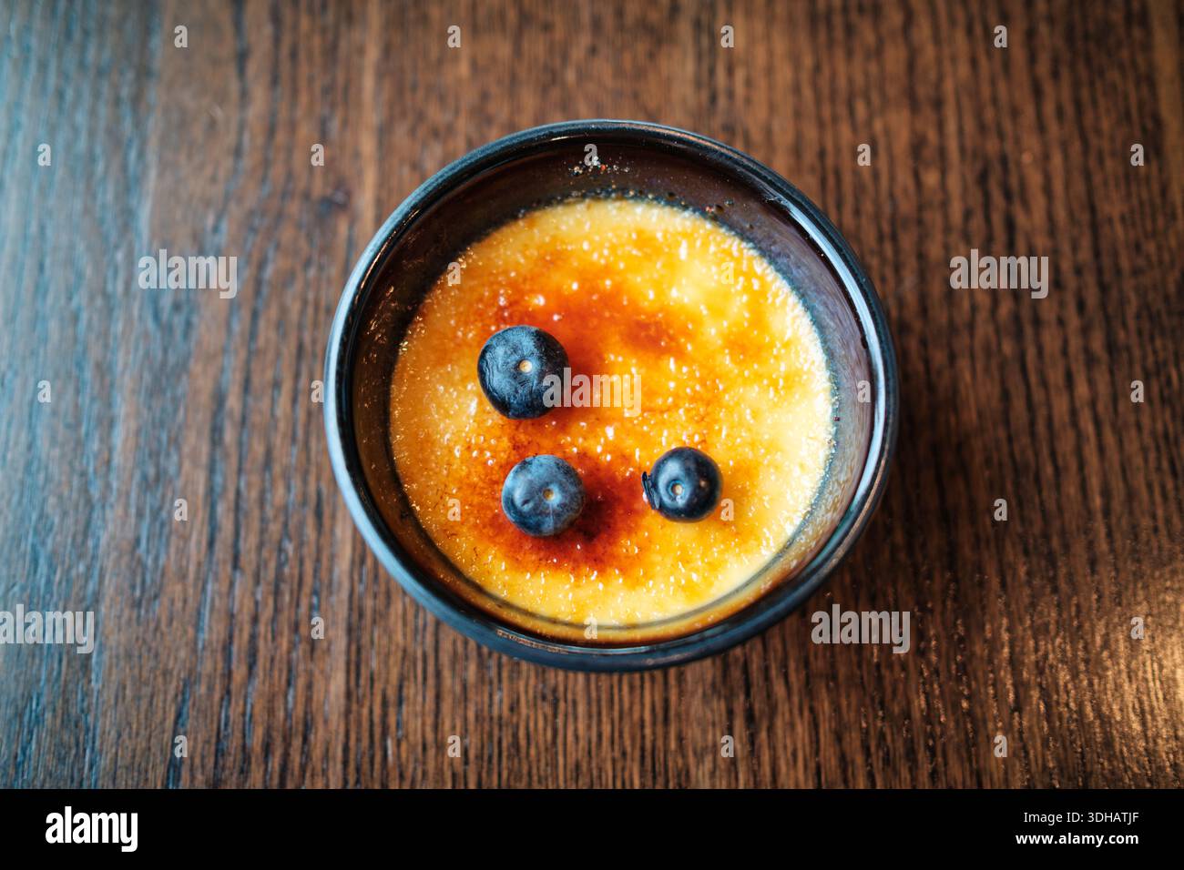 Vue de dessus du dessert français classique de Creme brulee avec croûte de sucre caramel et bleuet frais servi dans un bol sur une table en bois Banque D'Images