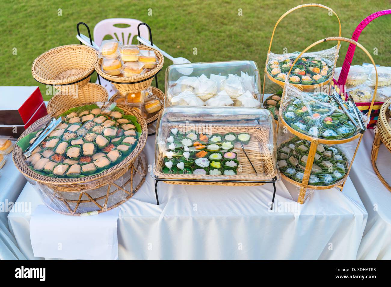 Divers desserts traditionnels thaïlandais et collations disposés dans un panier en bois, plateau en osier avec du plastique recouvert sur la table de buffet extérieure pour la restauration ou l'événement Banque D'Images