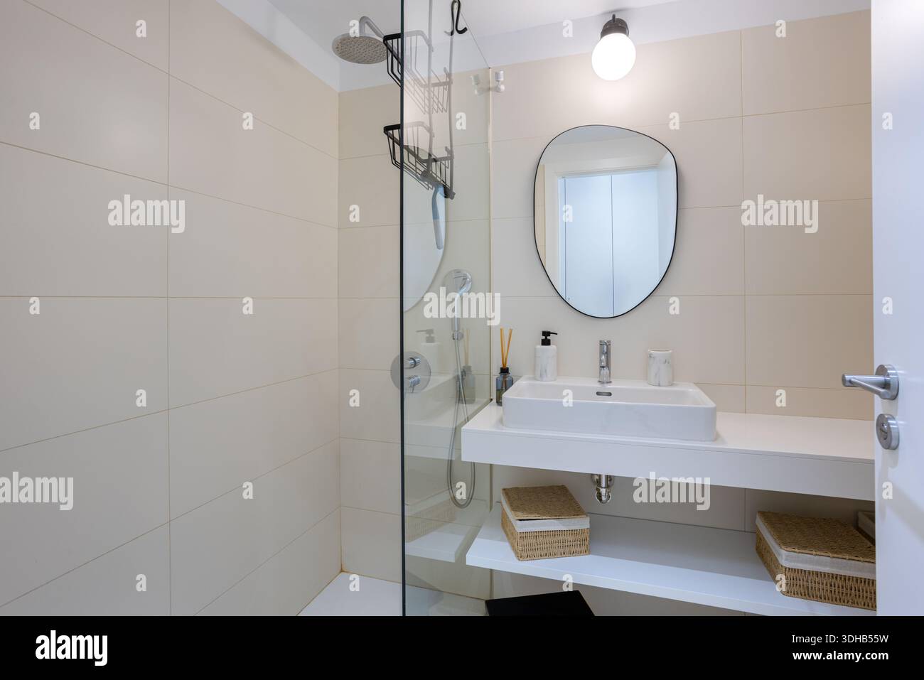 Salle de bains minimaliste avec miroir ovale, douche à l'italienne et paniers de rangement tissés sous l'évier Banque D'Images