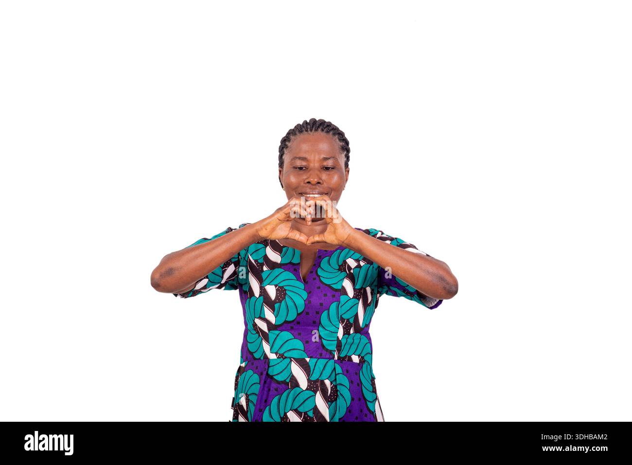 Belle femme africaine en robe de pagne debout sur fond blanc montrant le geste de coeur tout en souriant. Banque D'Images