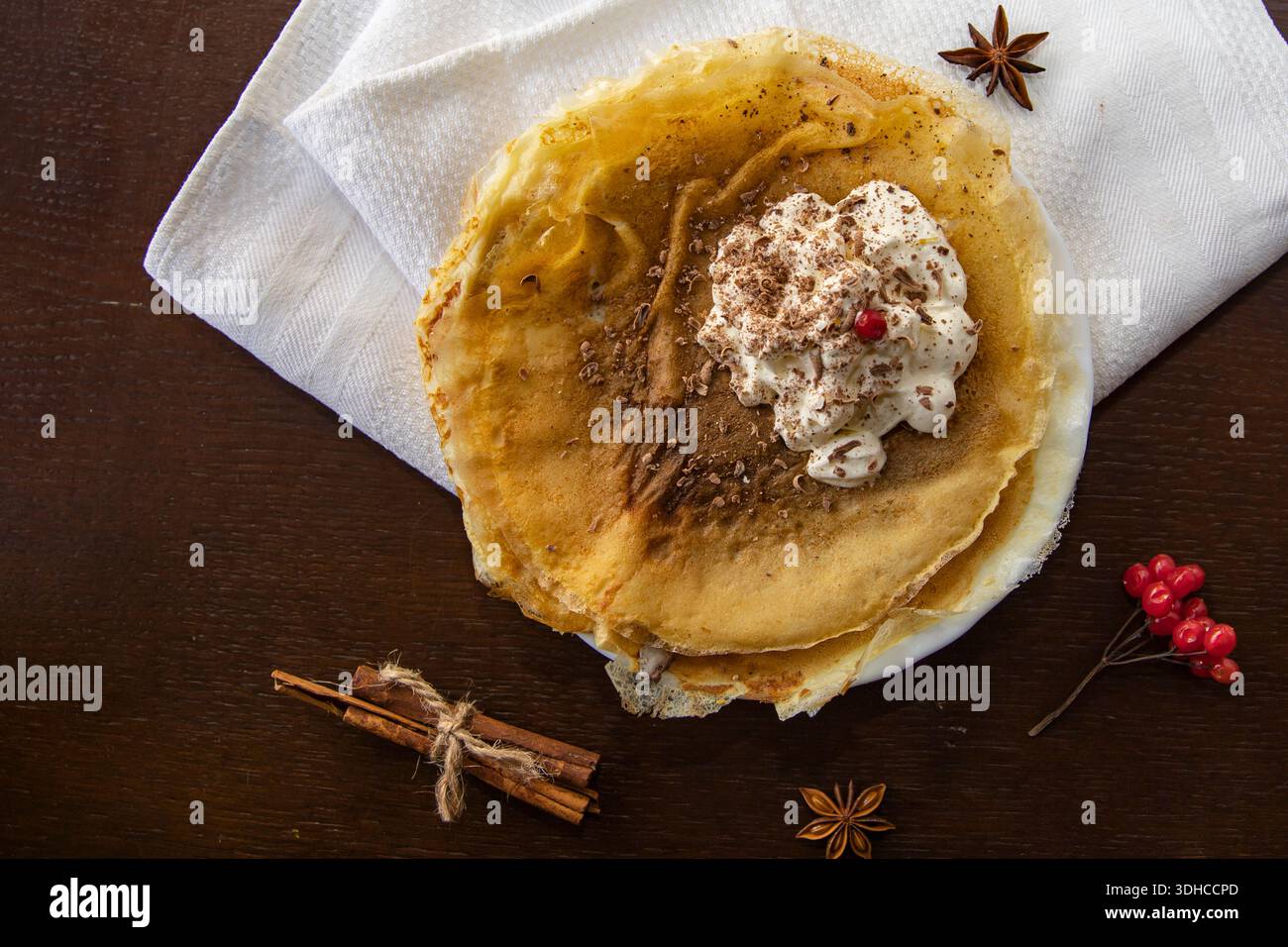 Crêpes fines avec cannelle à la crème fouettée et copeaux de chocolat sur une table en bois foncé Banque D'Images
