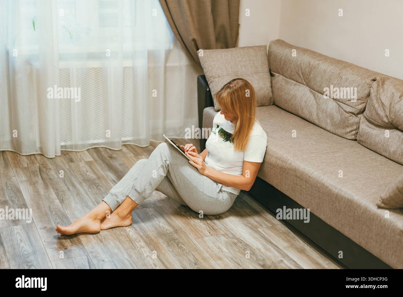 Femme assise sur le sol près du canapé à l'aide d'une tablette. Concept d'éducation en ligne, e-learning ou communication sur les réseaux sociaux. || autorisation du modèle Banque D'Images