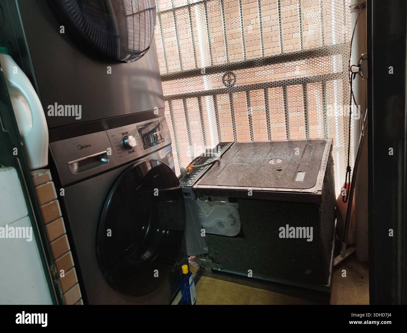 Ancien lave-linge et sèche-linge dans une buanderie encombrée avec fenêtre barrée Banque D'Images