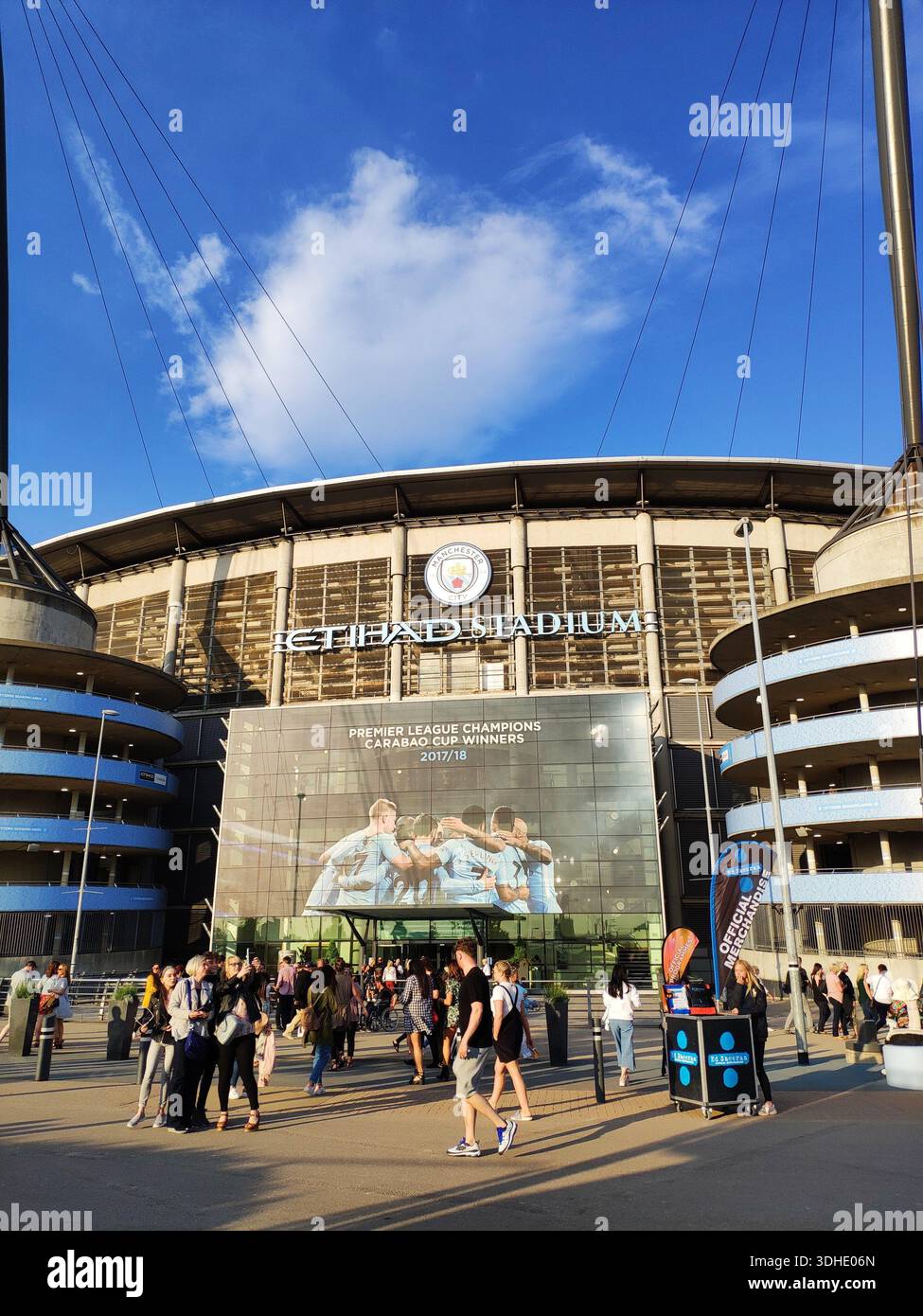 Extérieur du stade Etihad avec des fans marchant dehors sous le ciel bleu Banque D'Images
