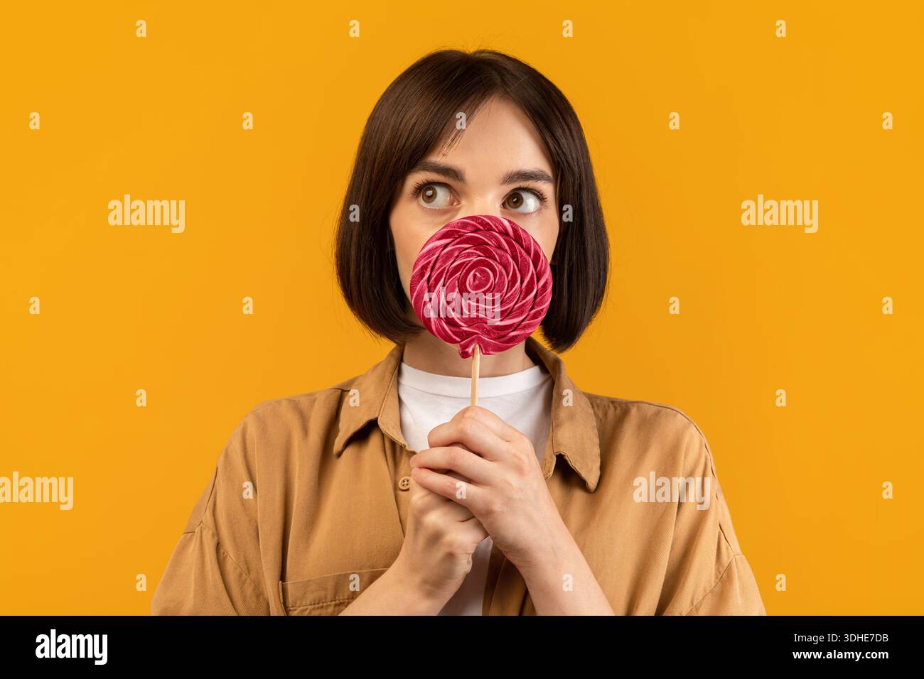 Concept de dent douce.Jeune femme espiègle caucasienne tenant le Lollipop, fermant et couvrant la bouche avec des bonbons sur le bâton Banque D'Images