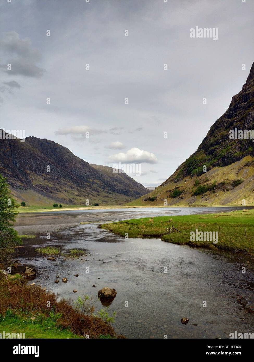 Un glen écossais serein avec une rivière sinueuse qui coule à travers des vallées verdoyantes sous un ciel nuageux Banque D'Images