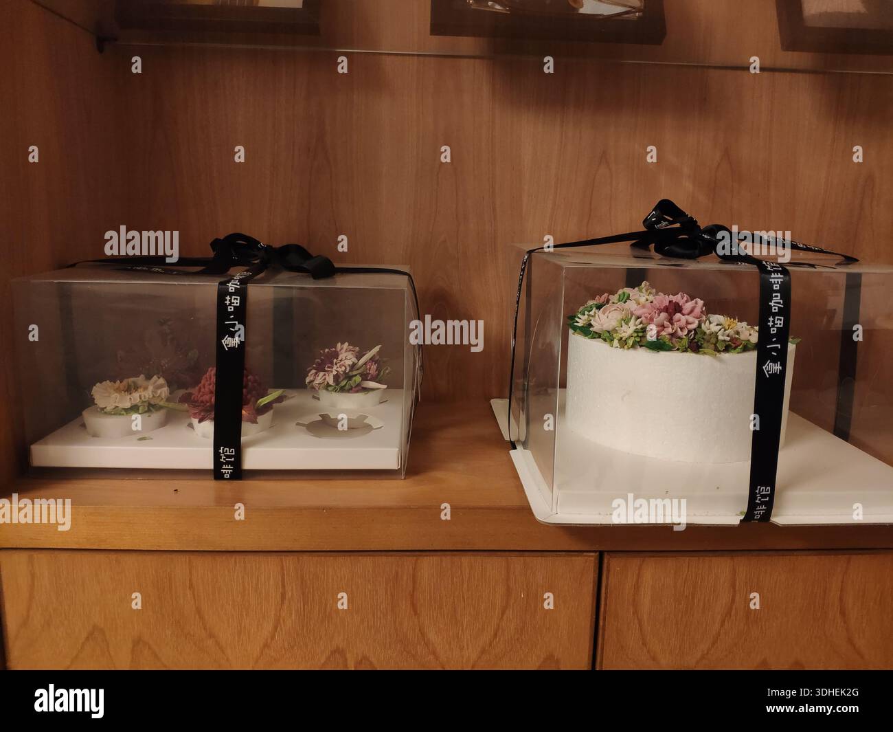 Gâteaux de mariage élégants dans des boîtes transparentes avec des rubans noirs sur une étagère en bois Banque D'Images