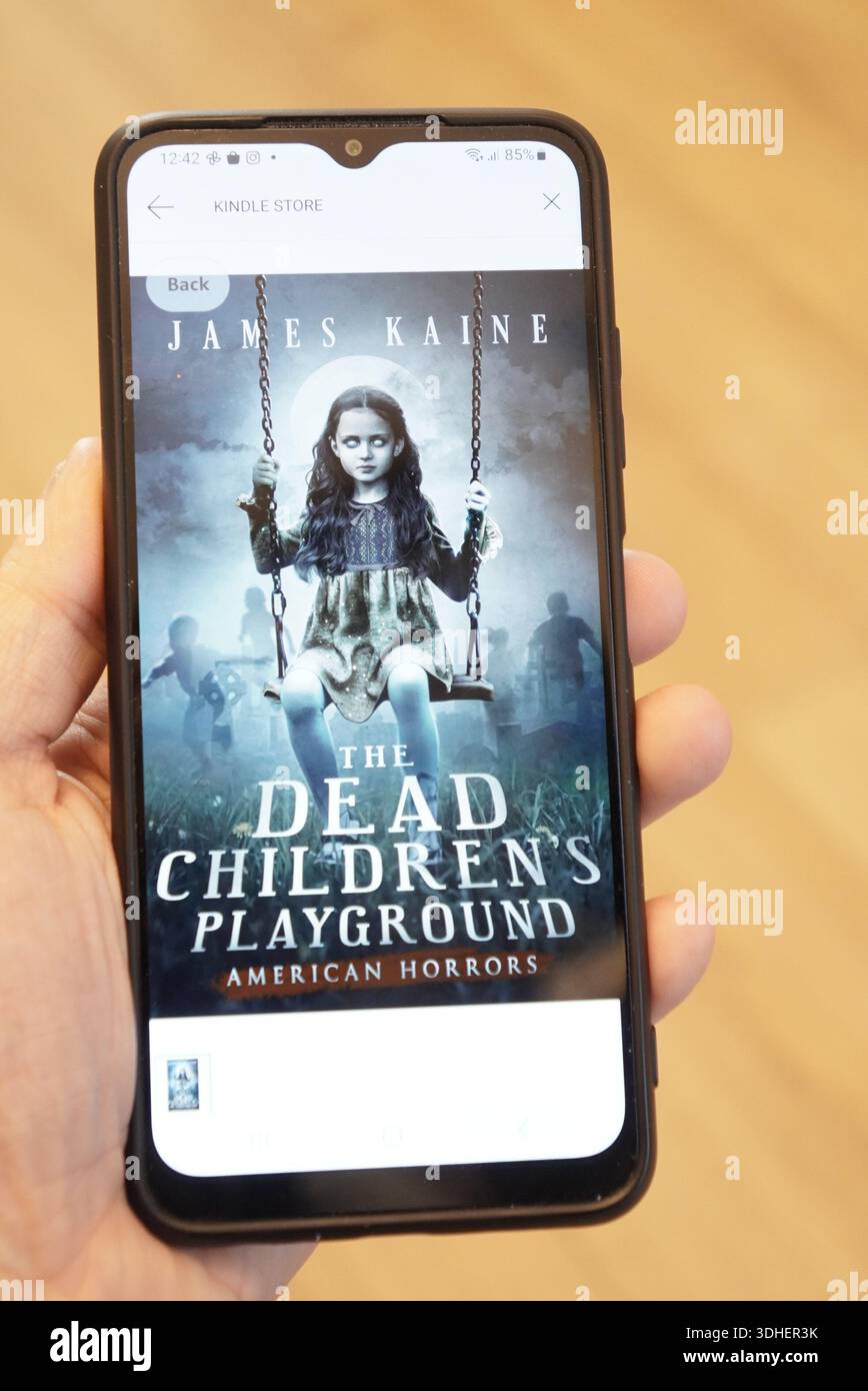 Smartphone tenant dans la main affichant la couverture du livre d'horreur « The Dead Children's Playground » Banque D'Images