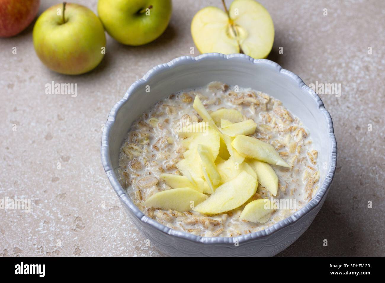 Bouillie de céréales multigrains à base de seigle, d'avoine, d'orge, de sarrasin et de flocons de blé, servie avec du lait et des tranches de pommes fraîches. Fond de pierre neutre Banque D'Images
