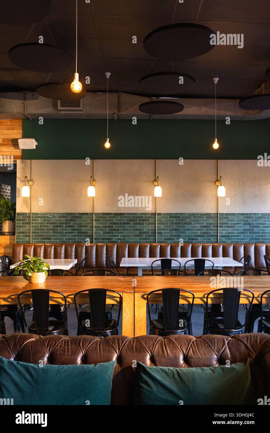 La table en bois commune couvre le centre avec des chaises en métal noir, un canapé touffeté, des carreaux de métro verts Banque D'Images