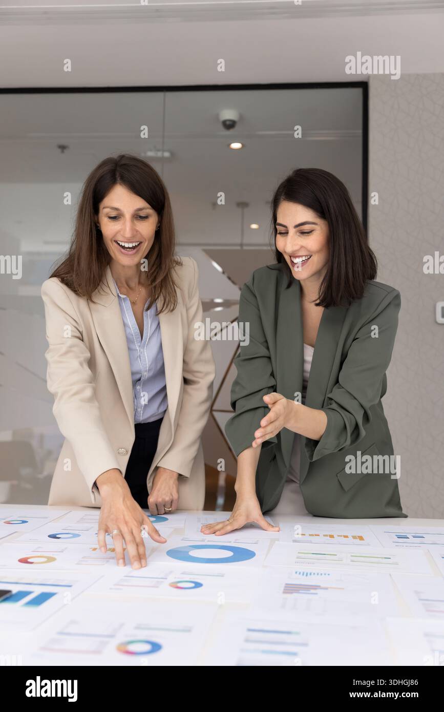 Deux femmes professionnelles heureuses examinant des tableaux et des graphiques imprimés Banque D'Images