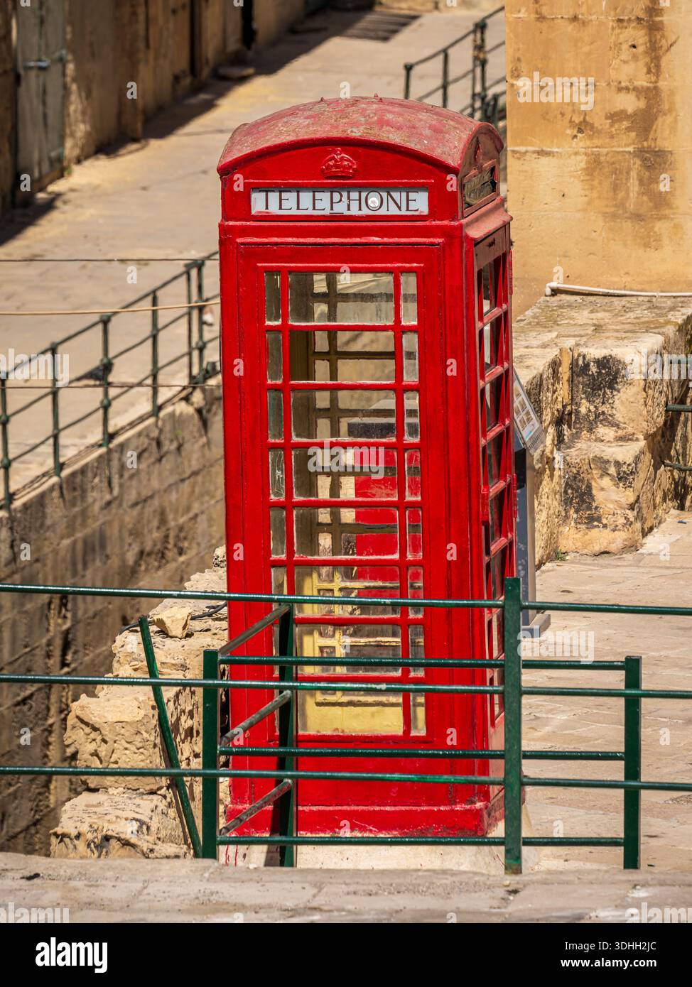 Une cabine téléphonique rouge traditionnelle debout à côté de murs en pierre altérée, créant un contraste visuel fort et une impression de patrimoine urbain intemporel Banque D'Images