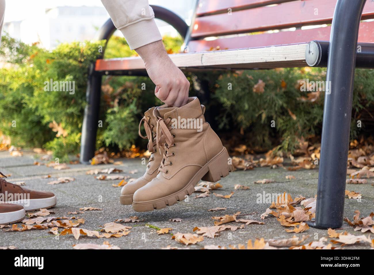 Gros plan de la main d'une personne tenant soigneusement des bottes de combat en cuir Havane élégantes avec une semelle épaisse résistante à crampons, parfaite pour la mode automnale polyvalente Banque D'Images