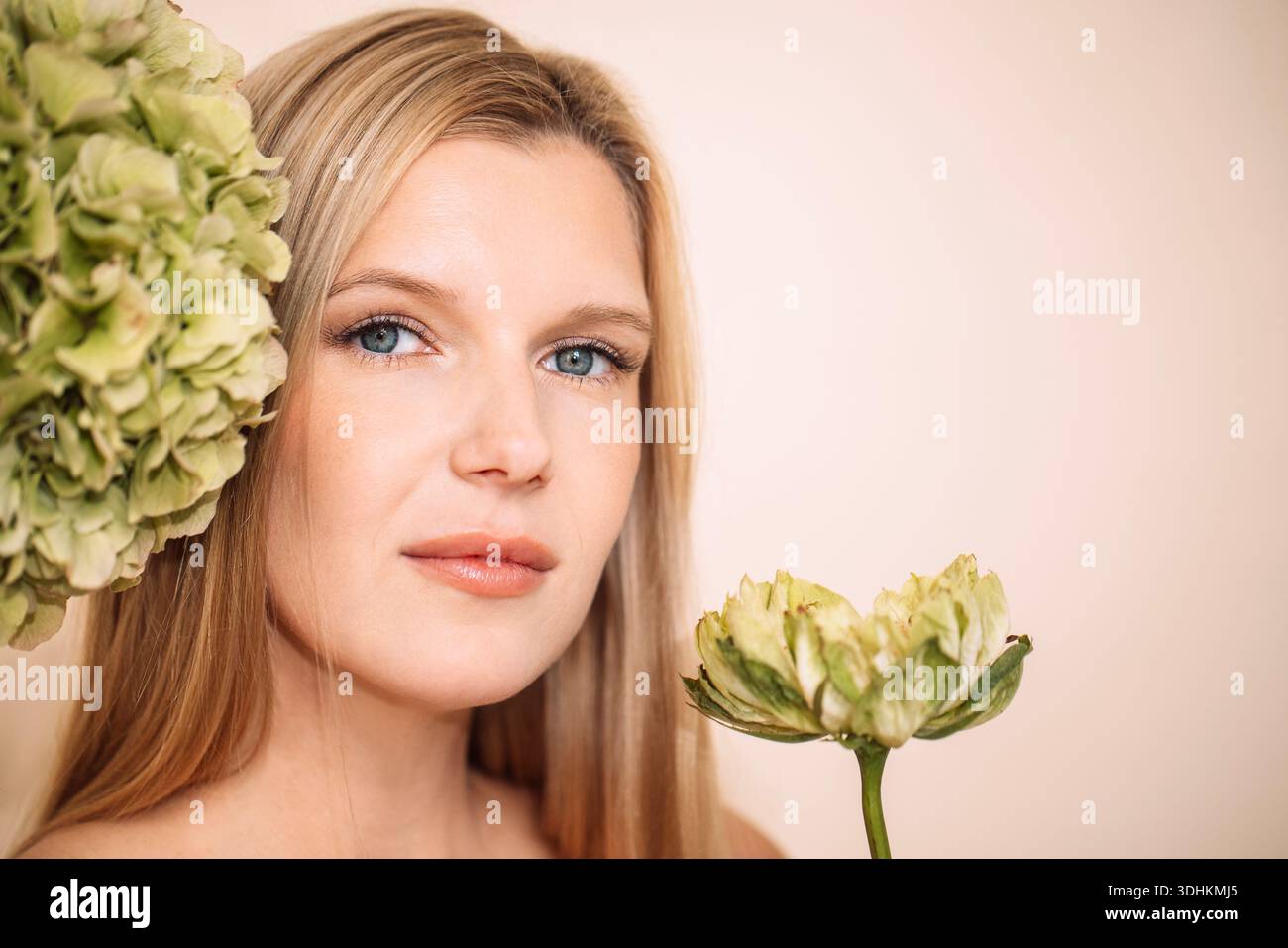 Modèle aux cheveux blonds, tenant la fleur verte, entouré d'arrangements floraux, soulignant la beauté naturelle et l'élégance dans une atmosphère calme et sereine Banque D'Images
