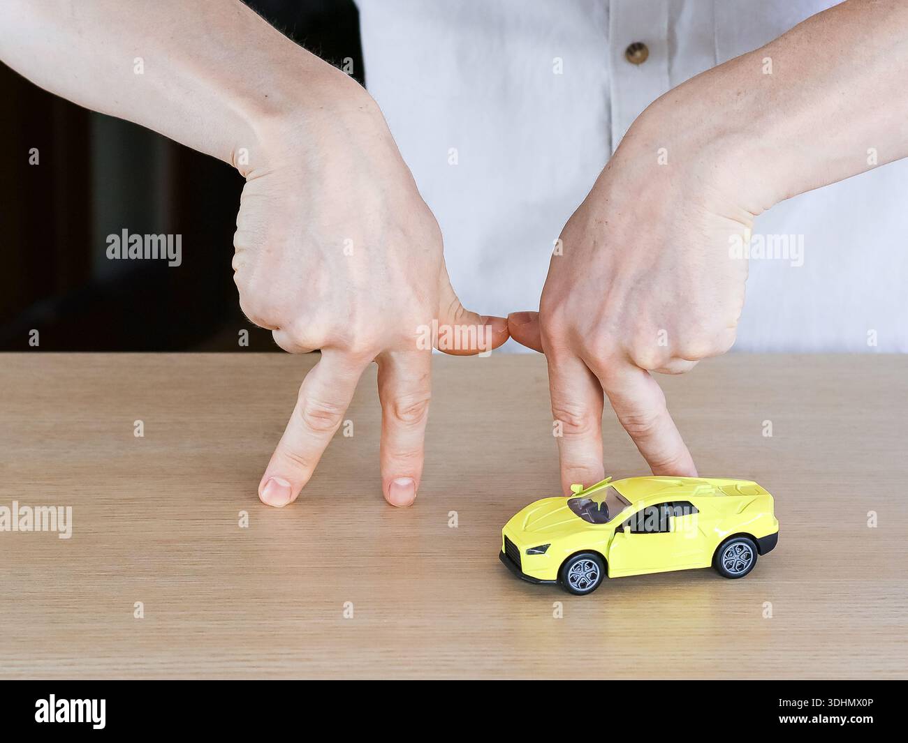 Gros plan des mains avec des doigts imitant des jambes approchant une voiture de sport jaune vif sur une table en bois. Banque D'Images
