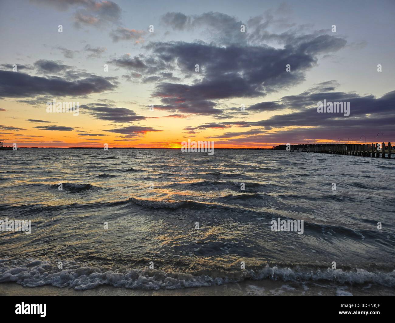 Coucher de soleil spectaculaire sur la baie de Rehoboth, Delaware, avec des vagues roulantes, des nuages colorés et une silhouette de jetée créant un paysage marin côtier tranquille - Image de stock capturée avec un smartphone