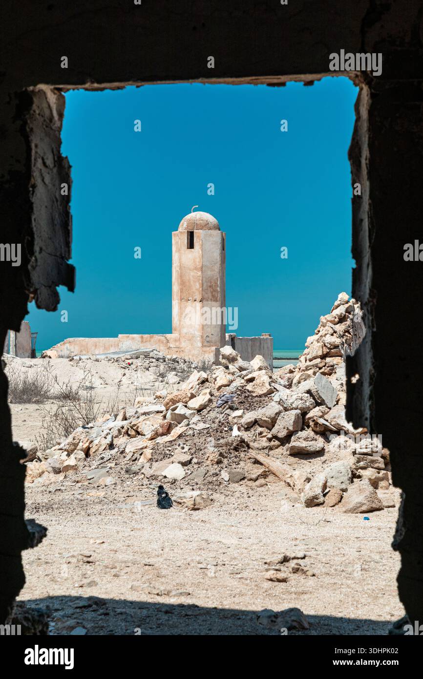 Al-Jumail, Qatar - 18 mars 2025. Une tour solitaire s'élève dans un désert désolé, encadrée par un mur en ruine. Des tas de gravats entourent la structure, un Banque D'Images