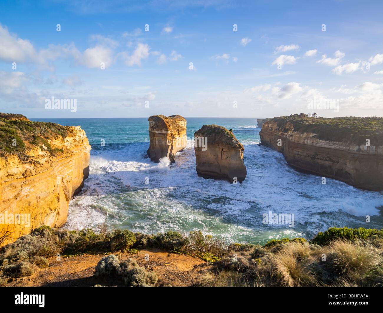Vue sur les falaises escarpées embrassent la mer turquoise, où la lumière dorée du soleil danse sur les vagues et les anciennes formations rocheuses se dressent haut, Lorne, Victoria, au Banque D'Images