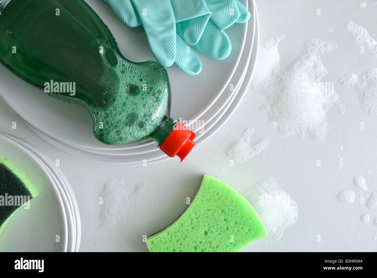 Vaisselle de lavage à la main fond avec pile de vaisselle et gants détergents et tampons à récurer sur le dessus sur un banc de cuisine blanc avec de l'eau et de la mousse. Haut vi Banque D'Images