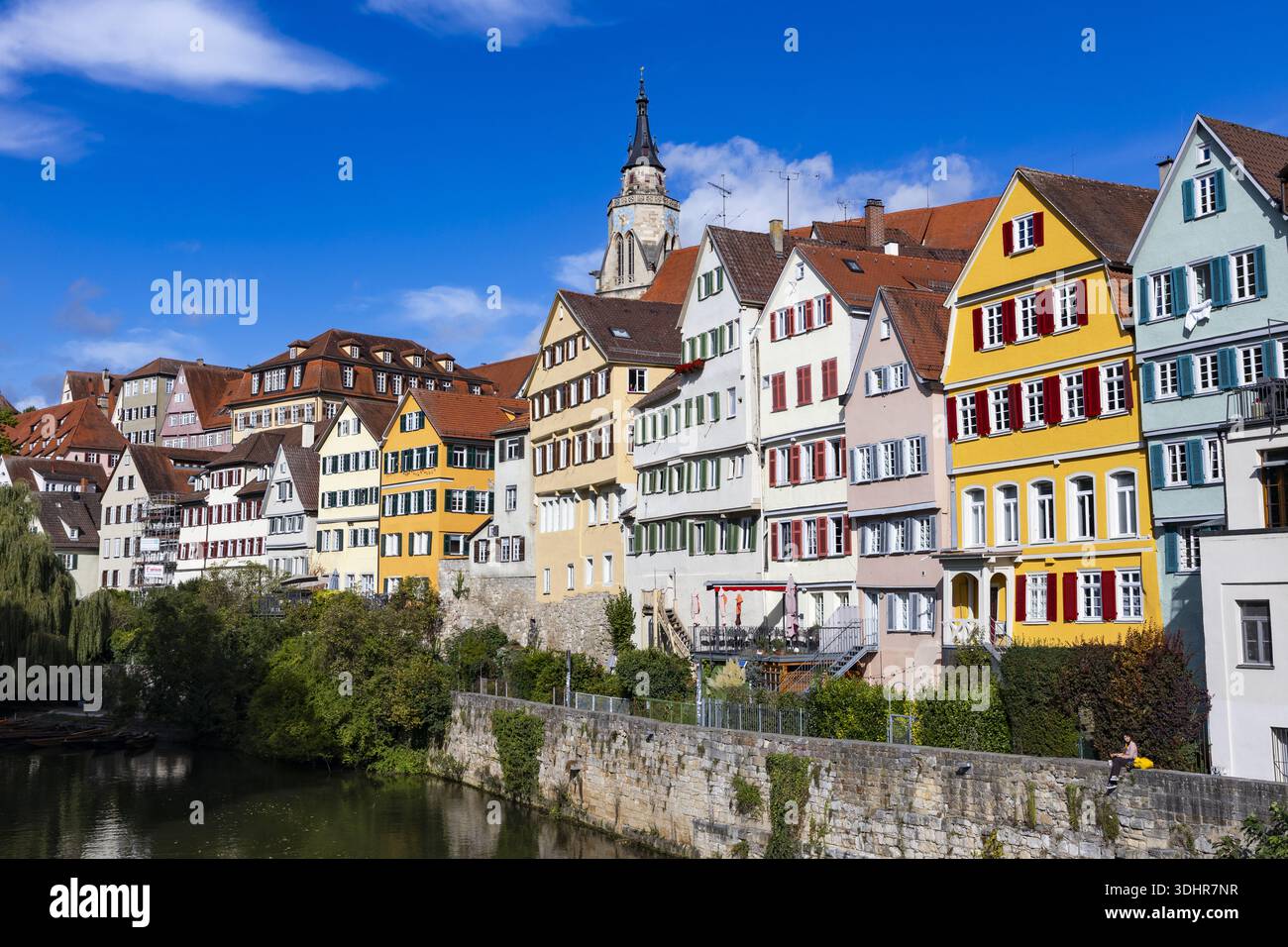 Vue de maisons colorées à colombages avec volets rouges bordent une rive sous un ciel bleu vif, une flèche d'église s'élève au loin, Tübingen, Ba Banque D'Images
