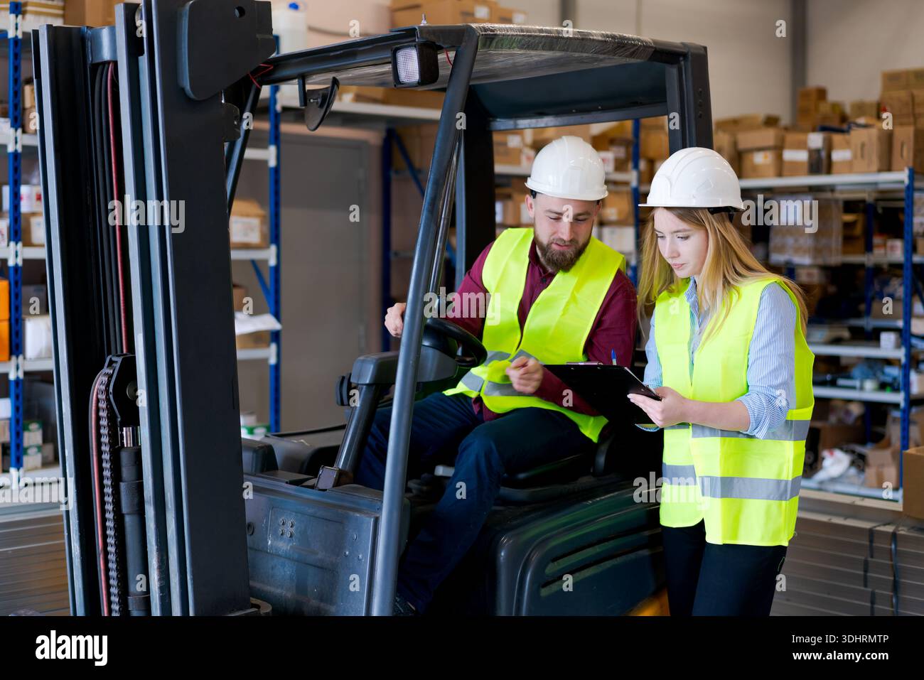Responsable logistique féminin avec planchette à pince donnant des instructions à un opérateur de chariot élévateur masculin. Équipe en équipement de sécurité gérant le stock et la distribution dans un mode Banque D'Images