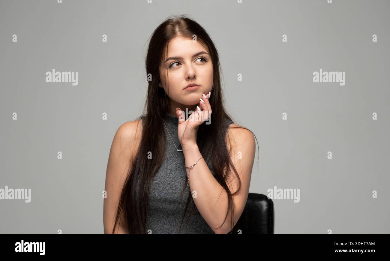 Jeune femme réfléchie regardant de côté avec la main sur le menton Banque D'Images