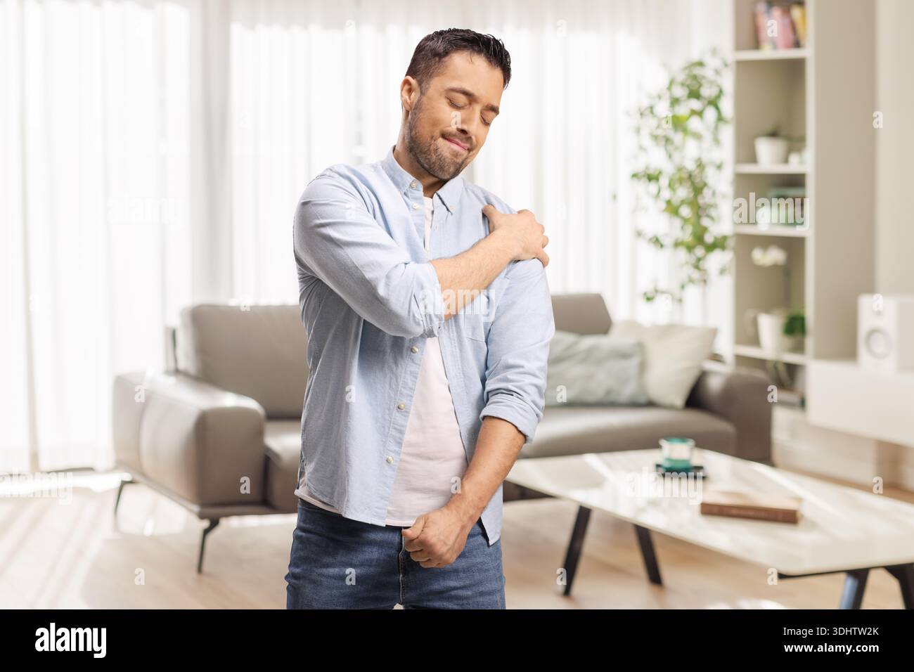 Jeune homme dans un salon touchant son épaule de douleur Banque D'Images