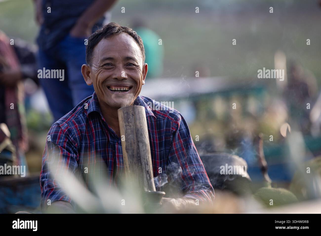 Rangamati, Bangladesh - 19 juin 2023 : vue du sourire radieux et des yeux chauds d'un homme local, tenant une pipe en bambou traditionnelle, au milieu du doux smo Banque D'Images