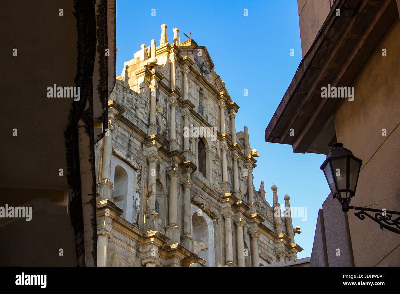 Vue en bas angle sur les ruines de la façade du Groupe Paul à Macao, présentant une architecture baroque en pierre sous un ciel bleu clair encadré par des bâtiments de la ville. Banque D'Images