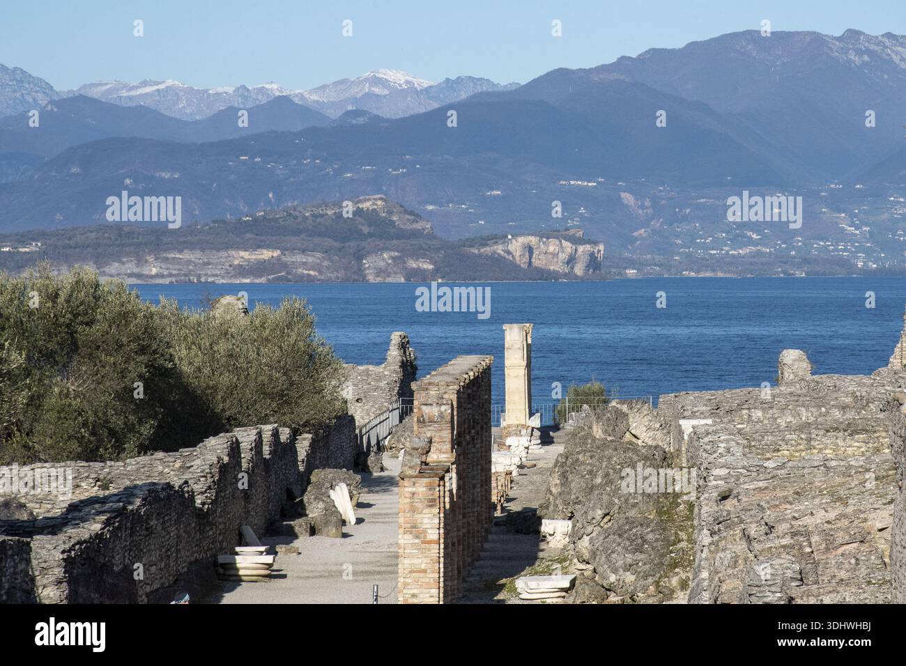 Vue sur les ruines antiques avec briques apparentes et murs de pierre menant aux eaux bleues brillantes d'un lac, encadrées par des montagnes lointaines, Sirmione, L. Banque D'Images