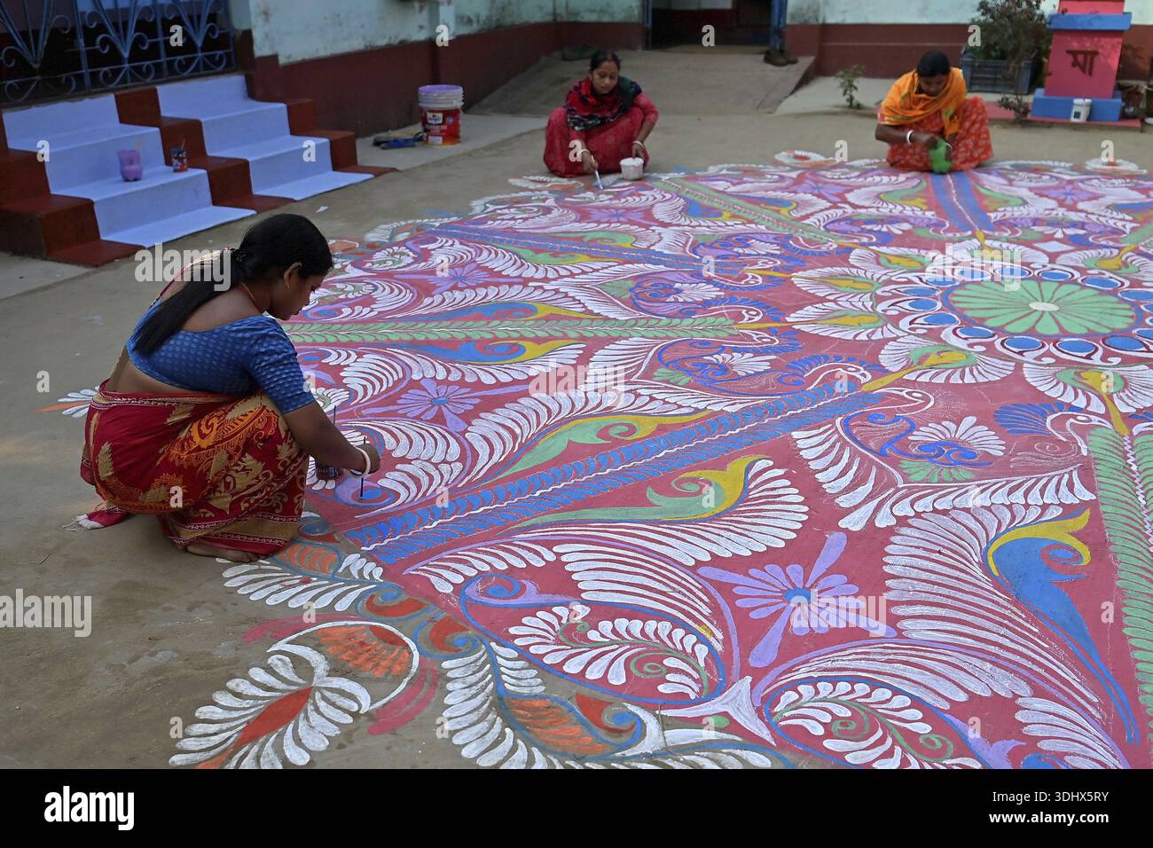 Agartala, Tripura, Inde, 12-01-2026 : des femmes peignent Alpona, sur le terrain avant le festival hindou Makar Sankranti dans le village de Lankamura à Agartala. Banque D'Images