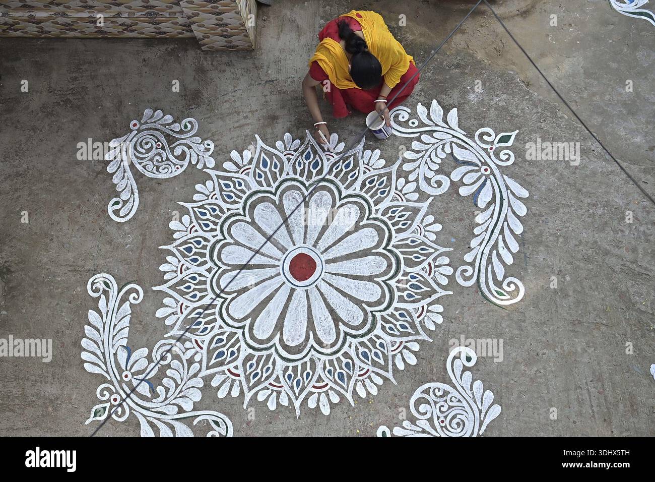 Agartala, Tripura, Inde, 12-01-2026 : des femmes peignent Alpona, sur le terrain avant le festival hindou Makar Sankranti dans le village de Lankamura à Agartala. Banque D'Images