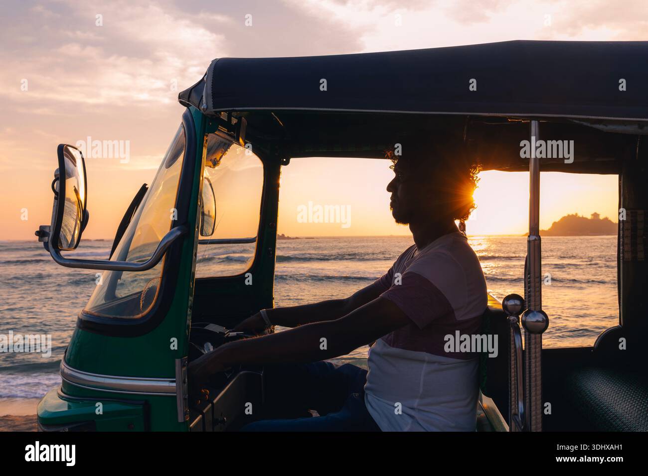 Silhouette de conducteur de tuk tuk conduisant le long de la route côtière pendant le coucher du soleil sur l'océan au Sri Lanka. Lumière dorée chaude, atmosphère tropicale et île emblématique tr Banque D'Images