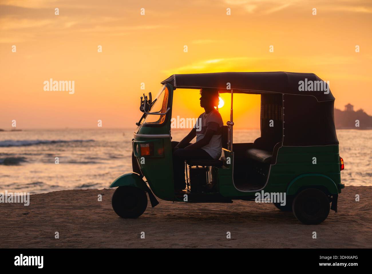 Chauffeur de tuk tuk local attendant à l'intérieur du véhicule sur la plage de sable fin pendant le coucher du soleil sur l'océan au Sri Lanka. Lumière chaude du soir et atmosphère tropicale calme. Banque D'Images