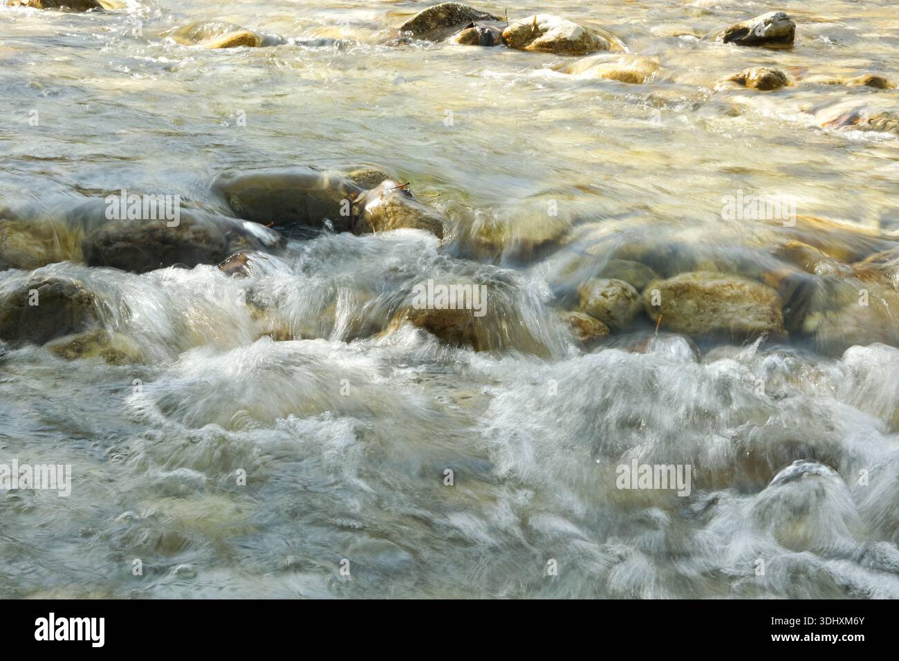 Fond d'eau abstrait dans Motion, River Stones Under Clear Flow. Banque D'Images