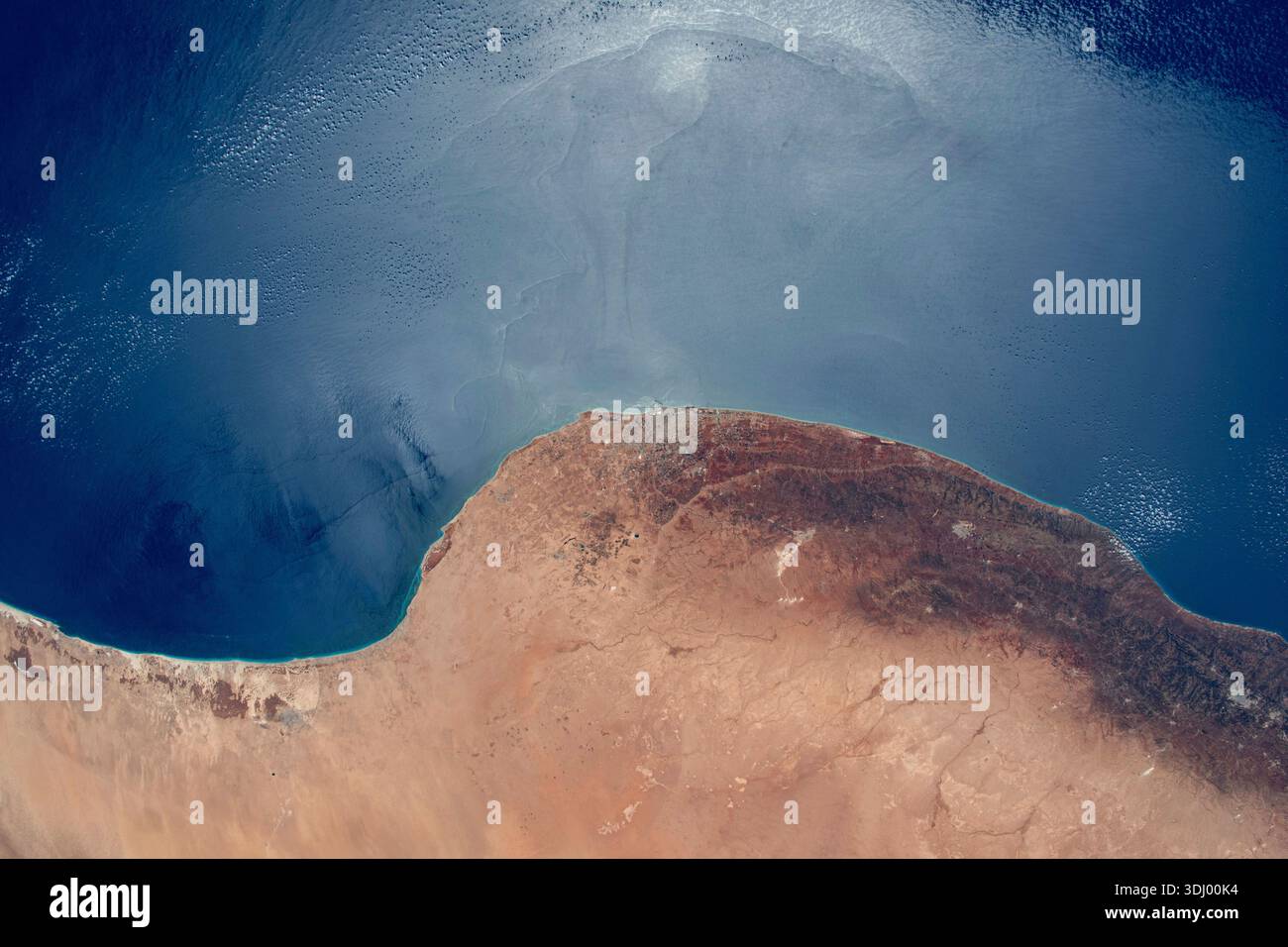 Le soleil scintille au large de la mer Méditerranée contrastant avec la côte désertique de Libye. Benghazi, une ville de 1,2 millions d'habitants, se trouve dans la région aride entre le désert et les climats tempérés. Photographie prise depuis la Station spatiale internationale le 4 août 2023. Une version optimisée d'une image originale de la NASA : crédit : NASA/WHoburg Banque D'Images