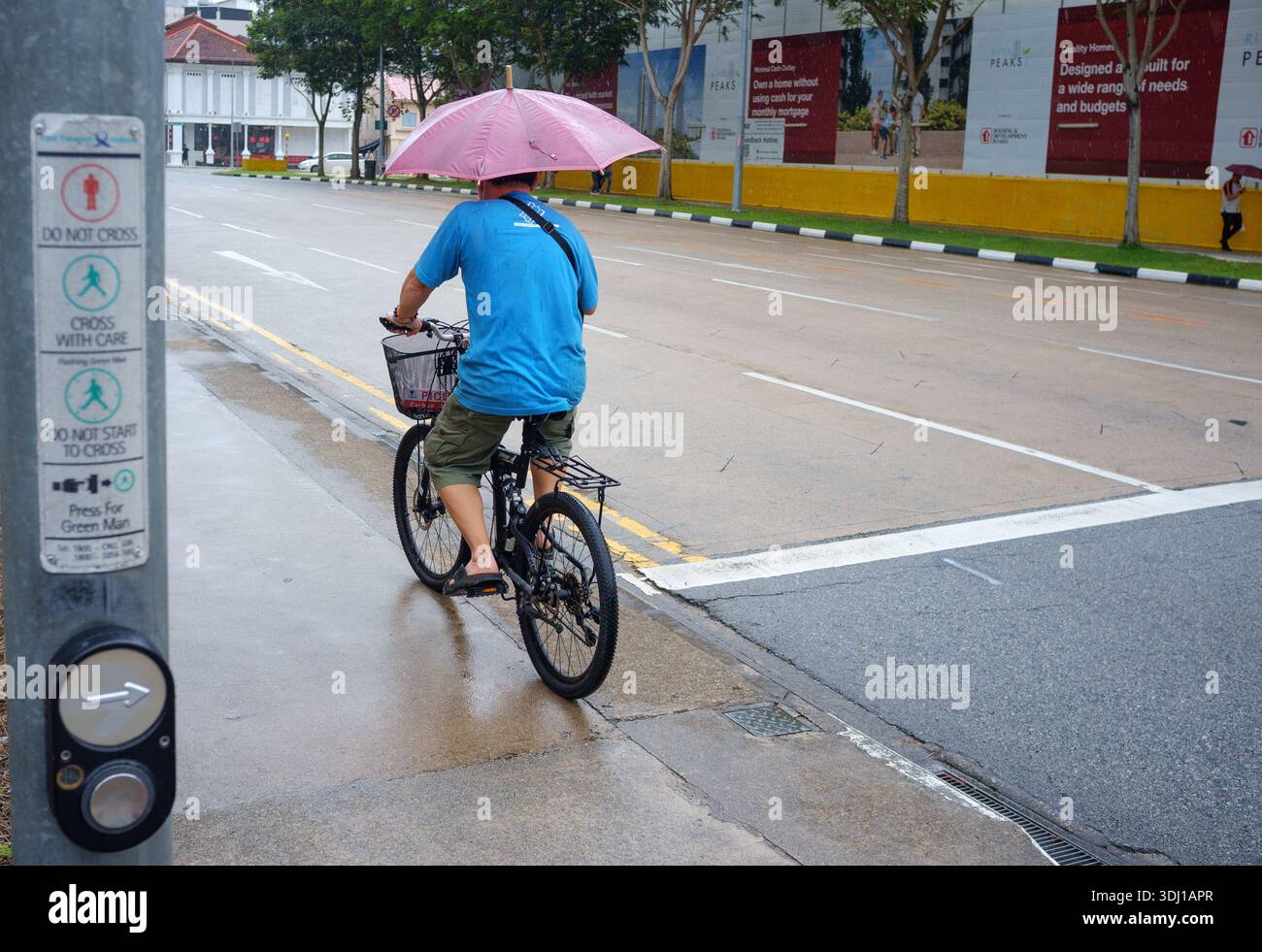 Un homme monte un vélo sur le trottoir tout en tenant un parapluie à l'abri de la pluie tropicale à Singapour Asie. Banque D'Images
