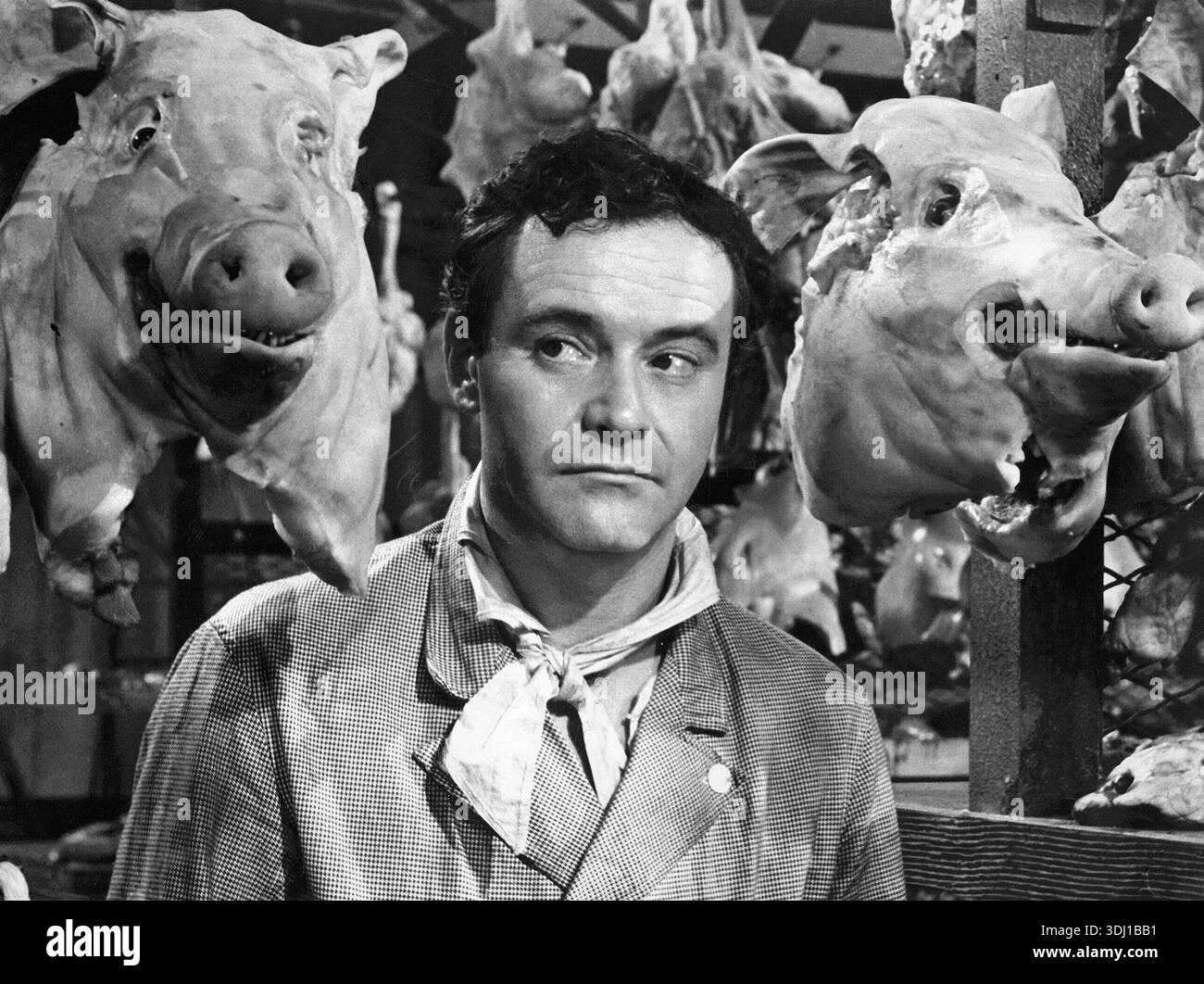 Cette photo noir et blanc du film de 1963 'Irma la douce' met en scène l'acteur Jack Lemmon dans le rôle de Nestor Patou, apparaissant contemplatif ou inquiet au milieu de têtes de porc suspendues dans une boucherie ou un cadre similaire. La scène capture un moment dramatique de la comédie romantique. Banque D'Images