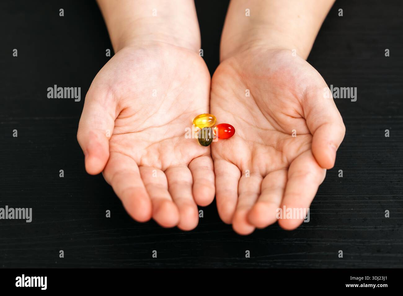 Les mains montrent trois capsules de gélatine de couleurs jaune, verte et rouge, placées sur une surface en bois foncé, soulignant les couleurs vibrantes des suppléments Banque D'Images