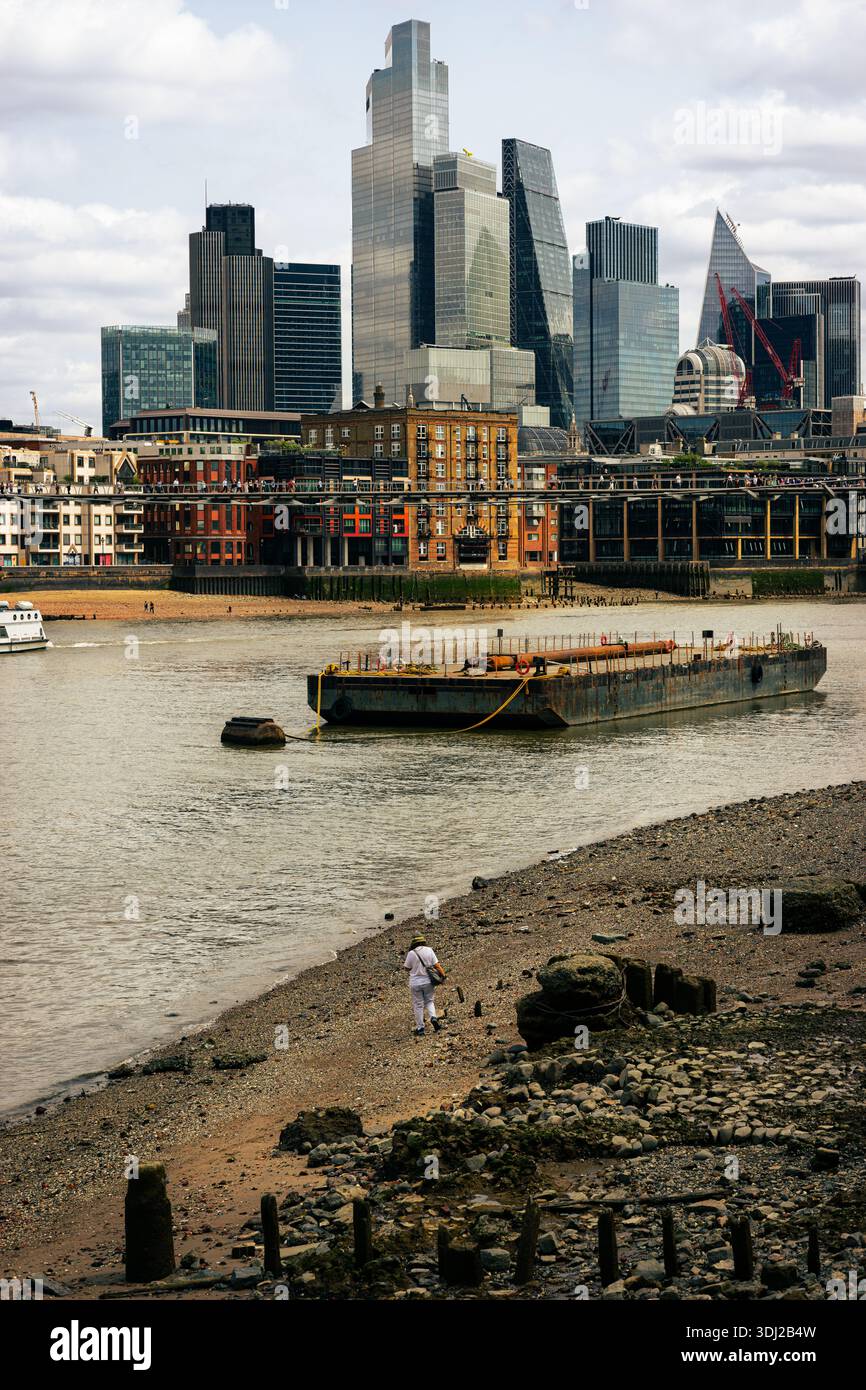 Un largueur de boue sur la rive sud passe devant une barge sur la Tamise tandis que les gratte-ciel de la City de Londres se dressent au loin Banque D'Images