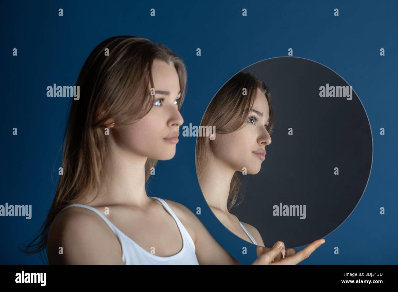 Jeune femme regardant son profil dans un miroir circulaire sur fond bleu Banque D'Images