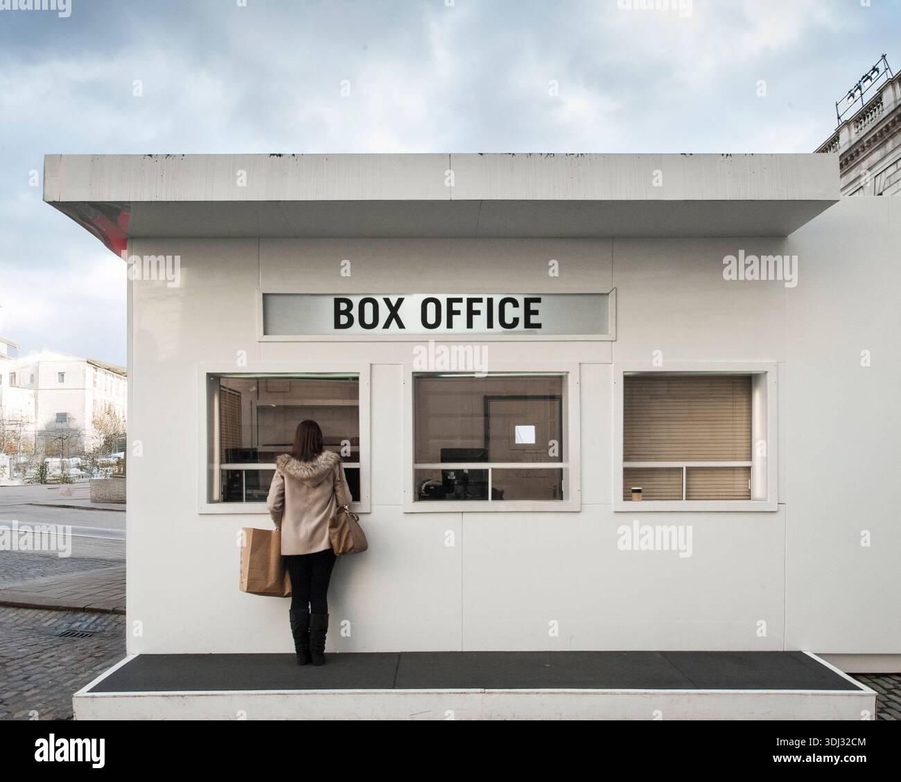Image conceptuelle d'une femme achetant des billets à un guichet minimaliste, mettant en évidence le comportement des consommateurs et les ventes de divertissement. Banque D'Images