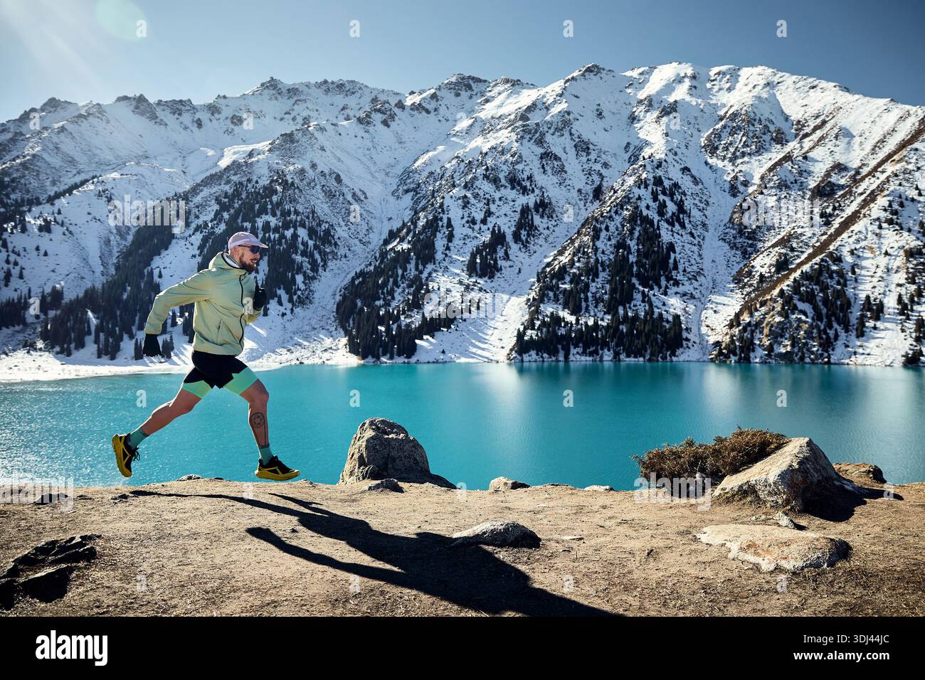 Homme athlète coureur sur le sentier dans la vallée de montagne à la journée ensoleillée d'hiver. Jogging en vêtements de sport à la nature. Banque D'Images