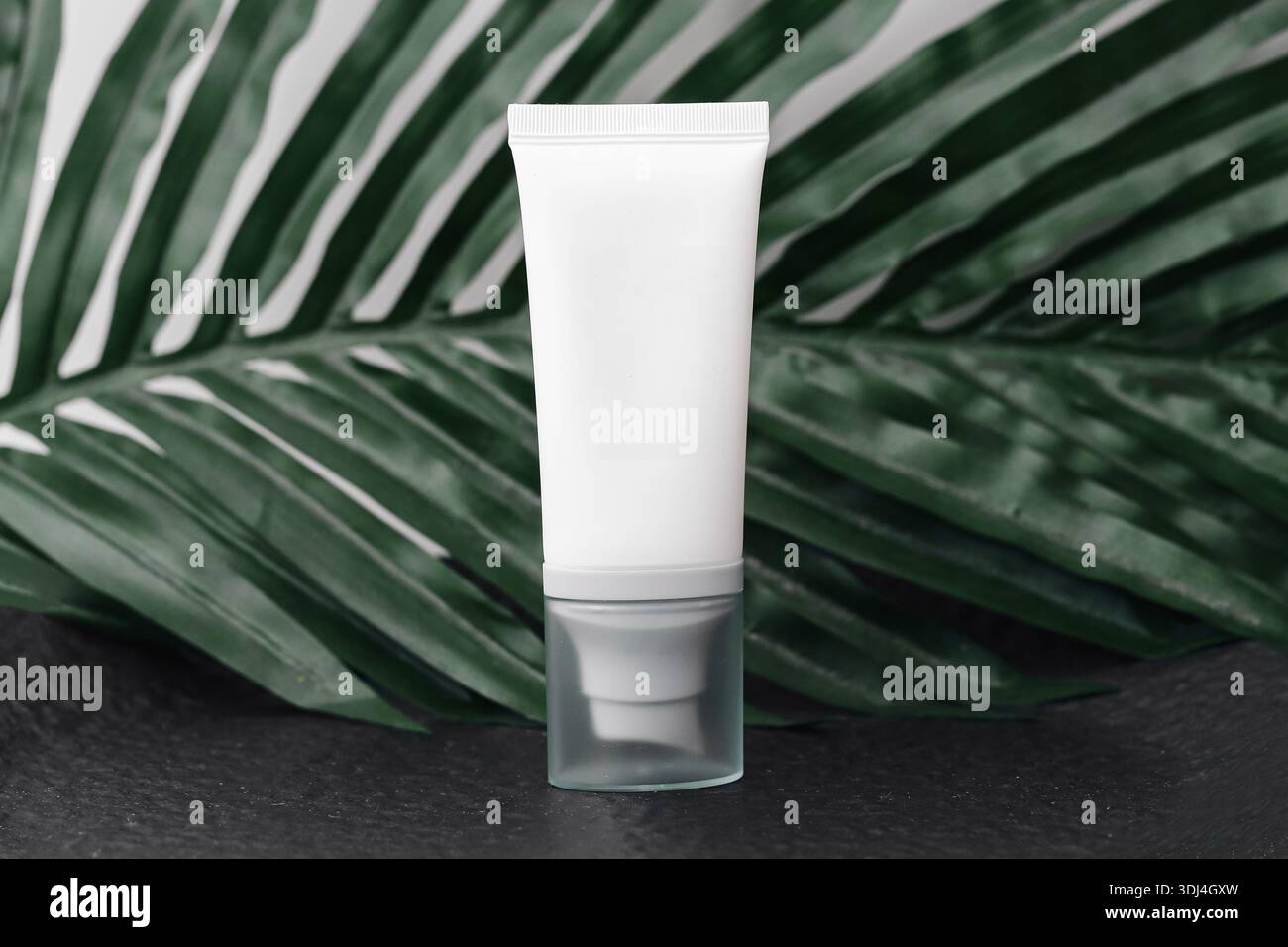 Maquette blanche de tube cosmétique sur fond de feuille tropicale verte. Emballage vierge pour produit de soin de la peau. Concept de marque de beauté minimal. Banque D'Images